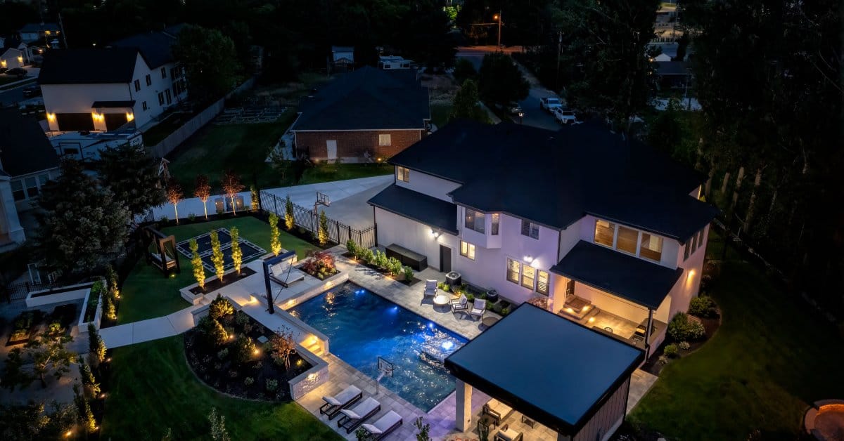 A nighttime view of a backyard pool in Utah. The pool has lighting accents surrounding the edges and cabanas.