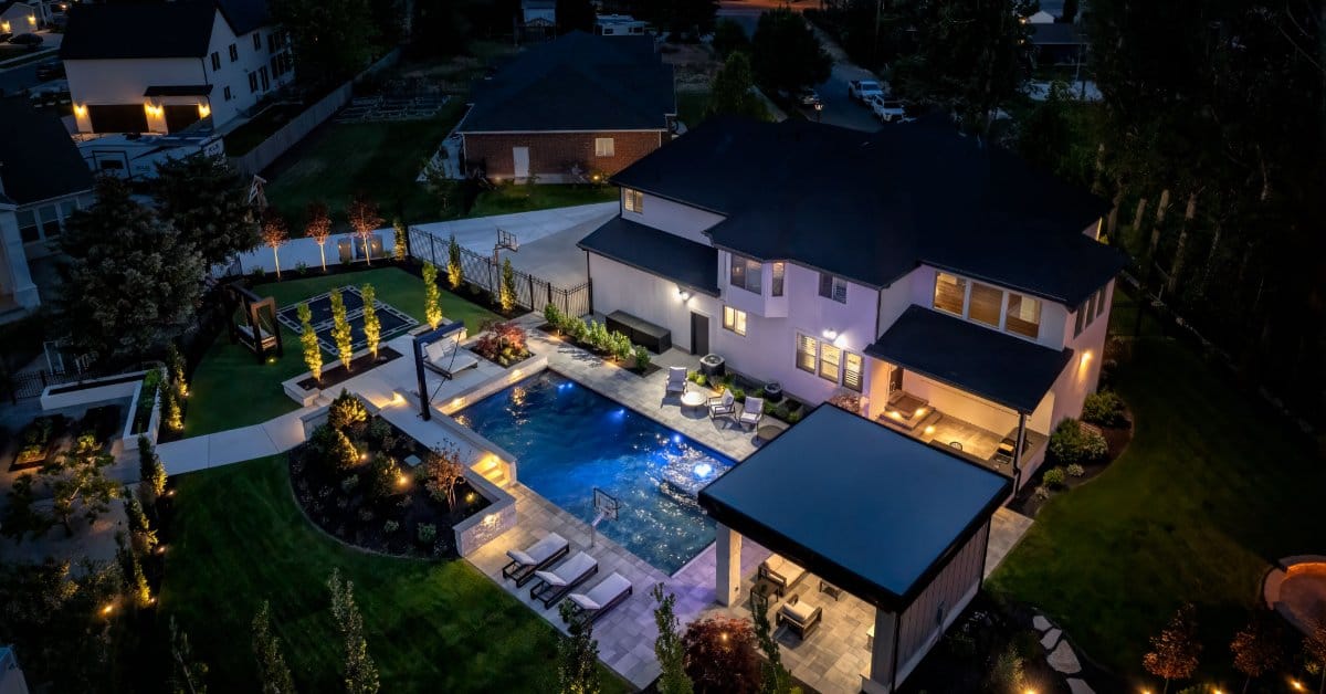 A luxury backyard at dusk with illuminated pool, lounge areas, and modern outdoor living space viewed from above.