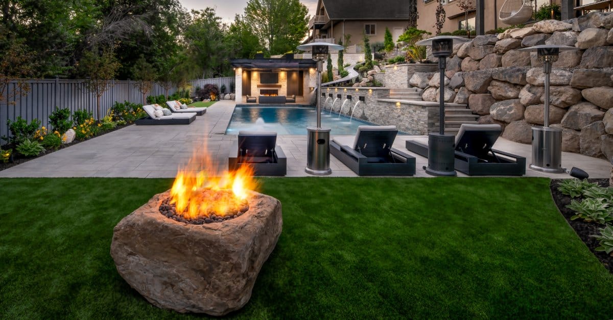 An elegant outdoor patio with fire pit, built-in grill, stone landscaping, and cozy seating for evening gatherings.