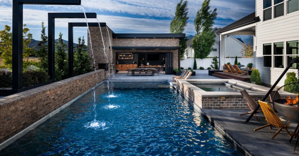 A luxurious in-ground pool with cascading water features, a spa, a fire pit, and a covered outdoor kitchen.