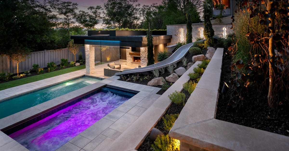 A multi-level pool space with the hot tub on the same level as the pool slide. The hot tub has a purple light.