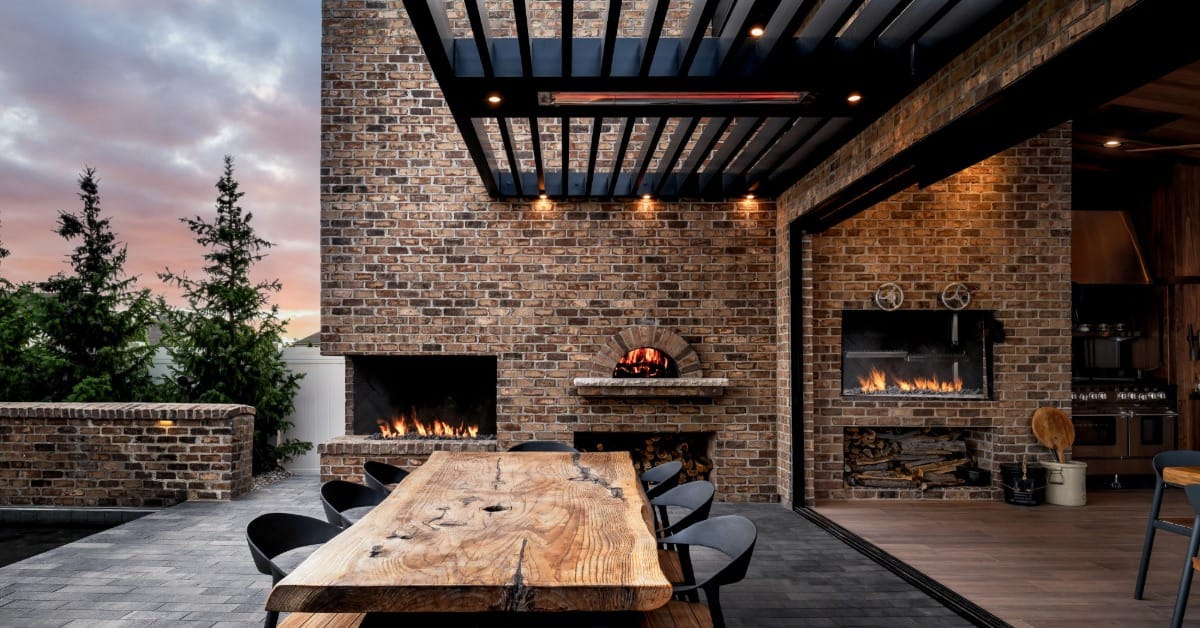 An outdoor entertaining area with exposed brick on the patio and a large table and chairs on the pavers. There's a fireplace.