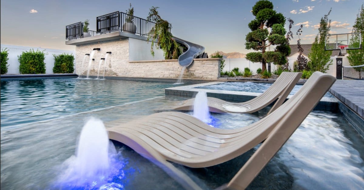 A close-up of two water chaise lounges on the pool ledge. There are smaller water features in between the chairs.
