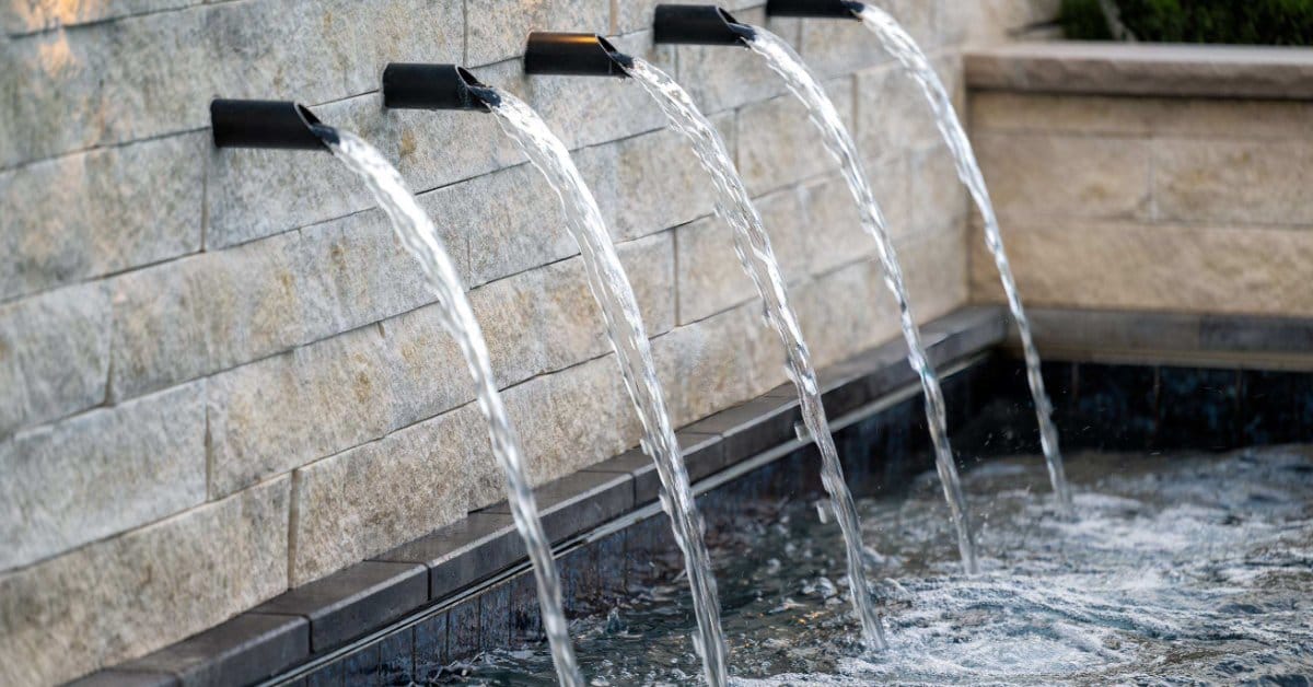 A series of five water spigots installed to a brick wall at the pool. The spigots drop the water into the luxury pool.