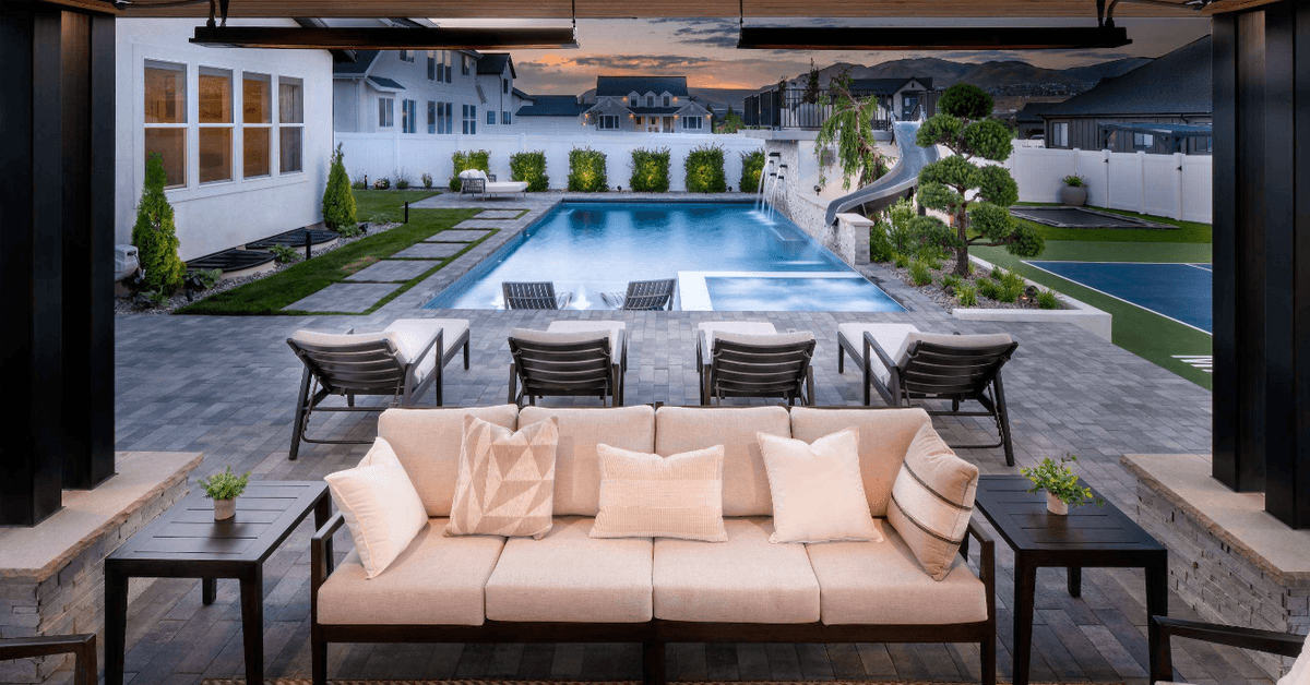An outdoor environment with high-end finishes, including a white couch in a pergola and a pool in the background.
