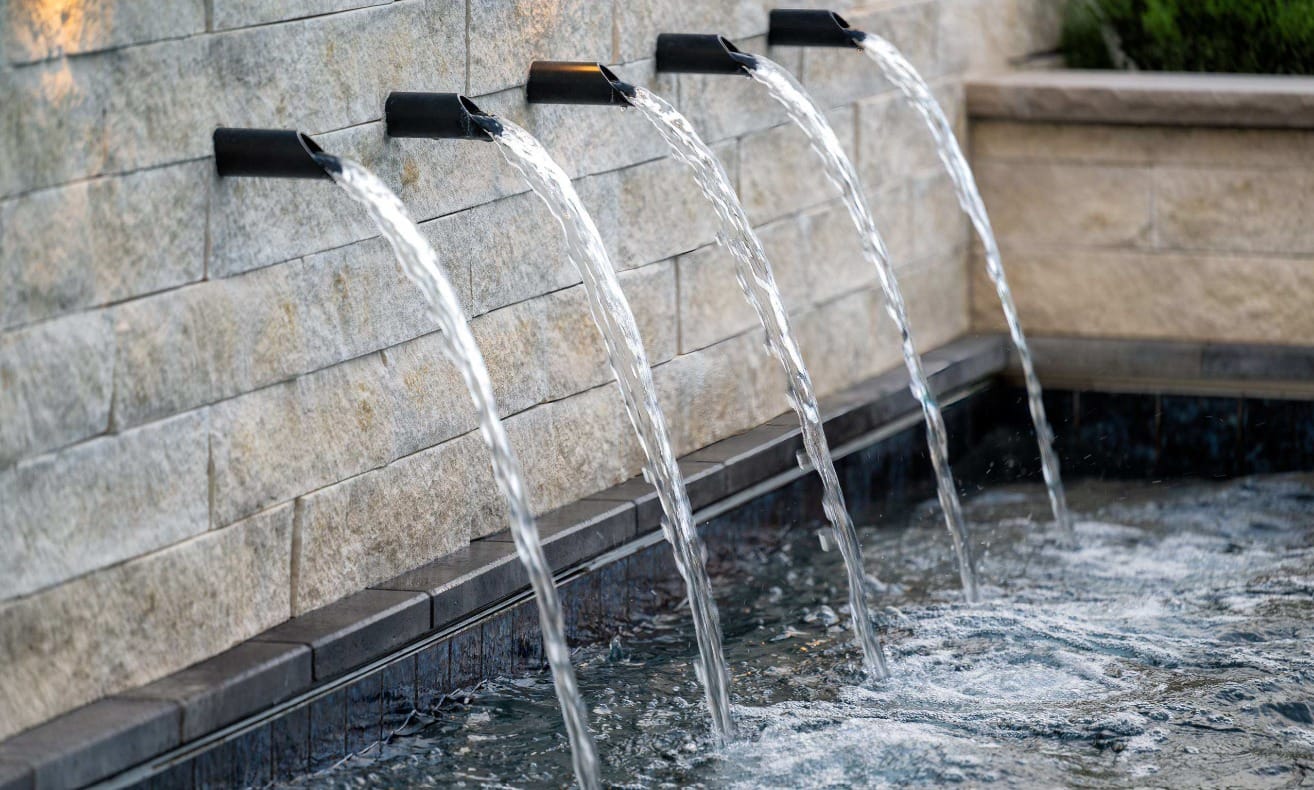 A luxury landscape water feature with five different spigots in a row with water flowing out into a reservoir.
